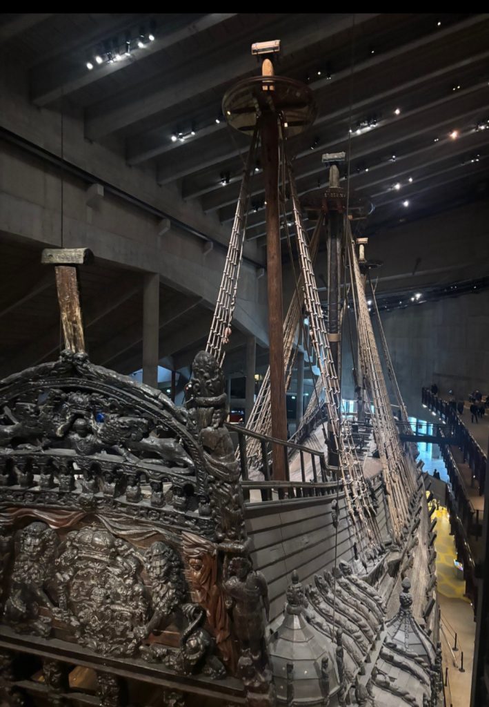Vy av det historiska skeppet Vasa inifrån Vasamuseet, med detaljerad träutsmyckning på akterspegeln och riggen som sträcker sig uppåt.