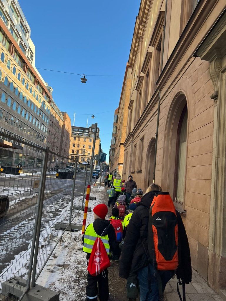 En grupp barn med reflexvästar går på led i stadsmiljö