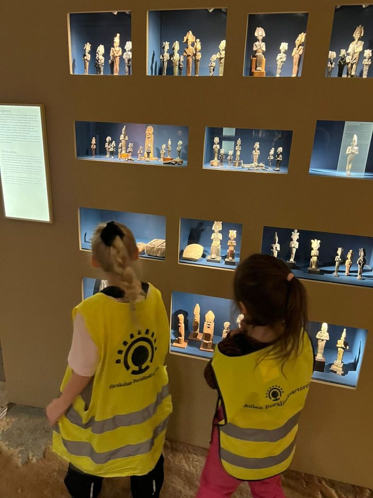 Två barn med reflexväst tittar på gamla antika statyetter som står bakom glas.
